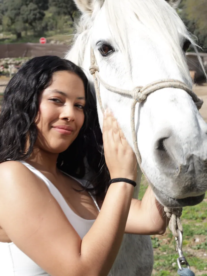 Una visitante sonríe apoyada en un caballo blanco en Finca El Sarao
