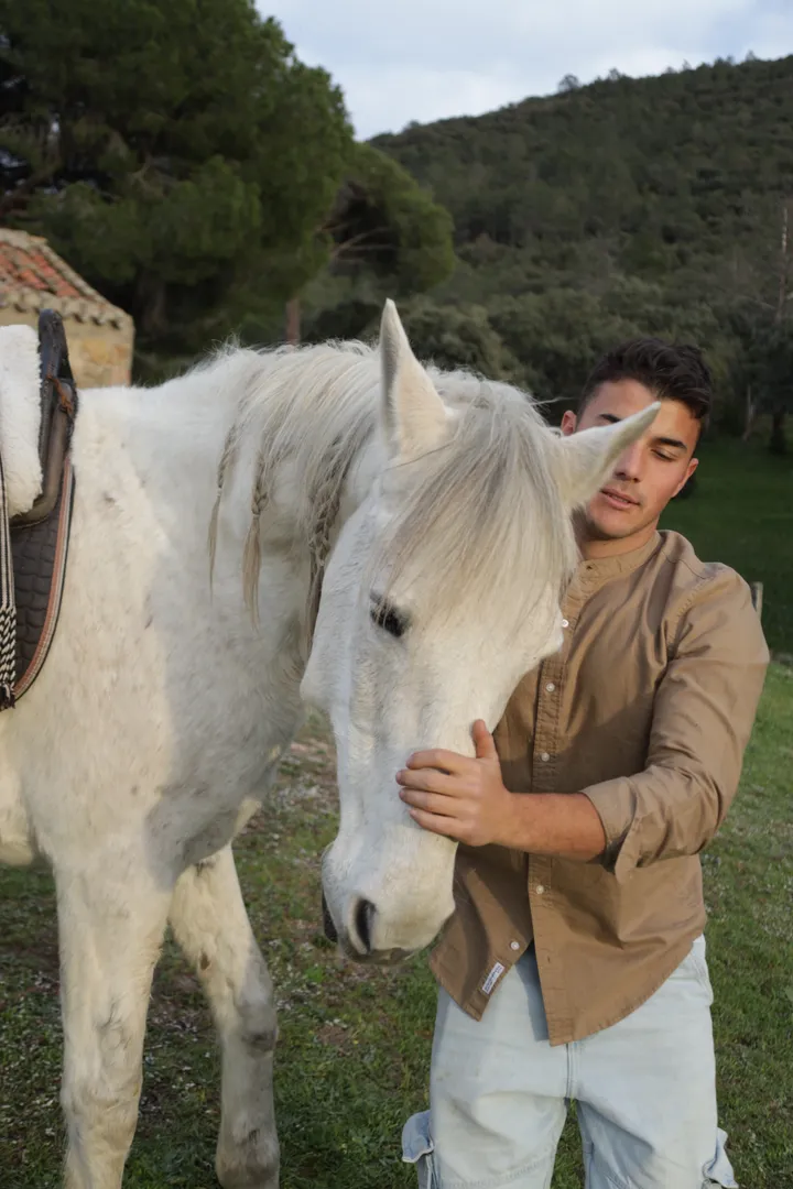 Un joven acaricia el morro de un caballo blanco en Finca El Sarao